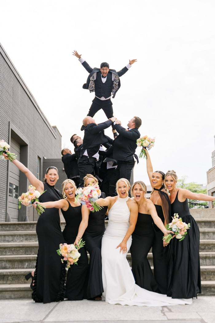 Wedding party celebrating, lifting the groom in his ABR tuxedo above their heads
