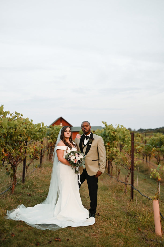 Bride and groom among the vines — groom in a champagne dinner jacket with black shawl lapel