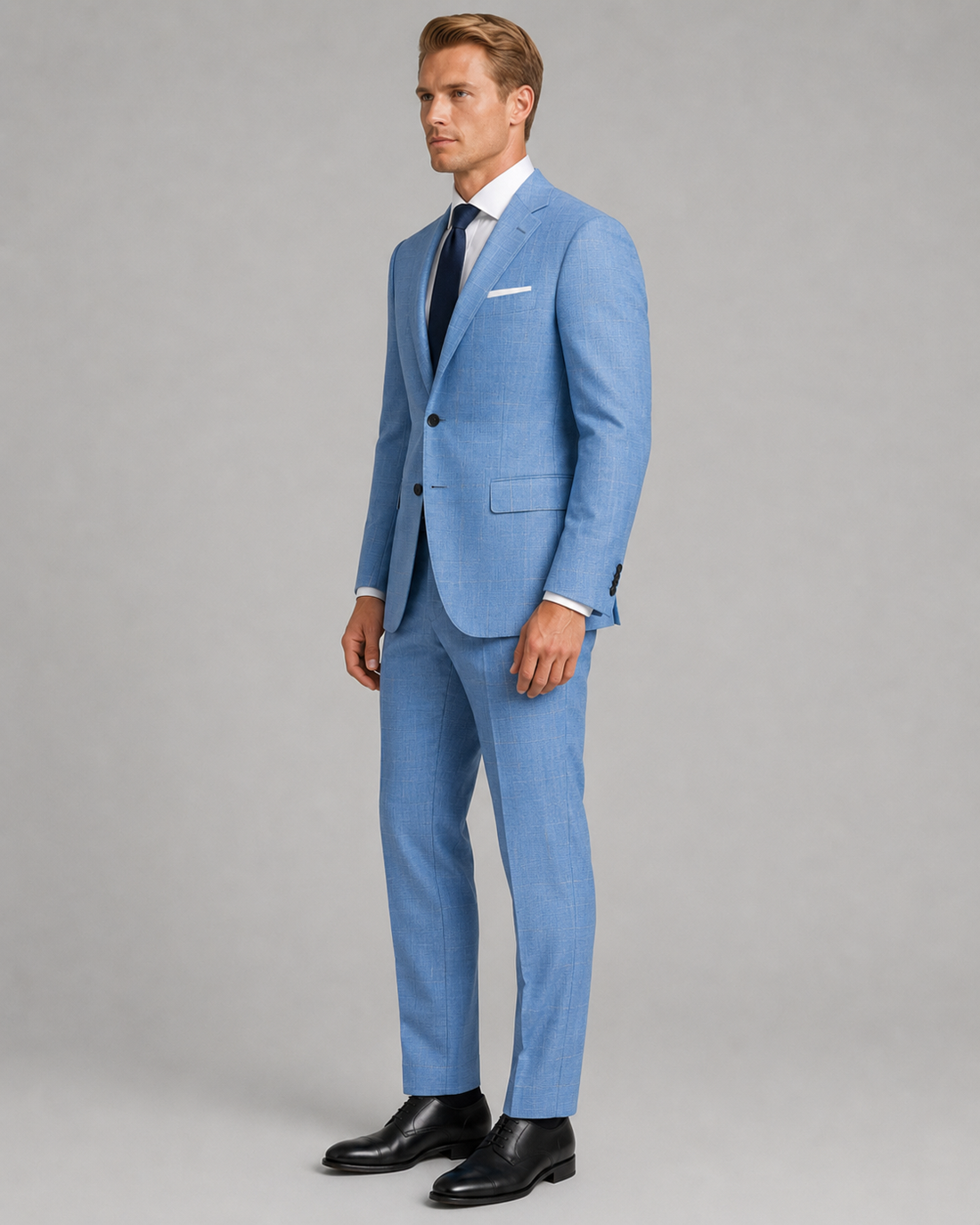 Man wearing a light blue suit with a white shirt and black shoes on a gray background