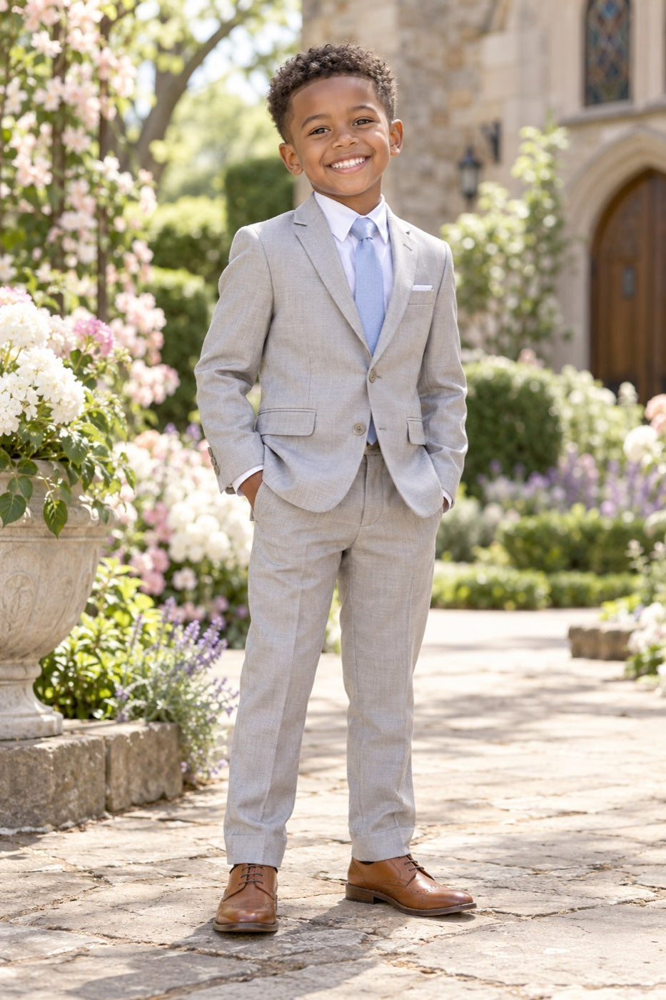 Smiling boy in a light grey suit among spring flowers